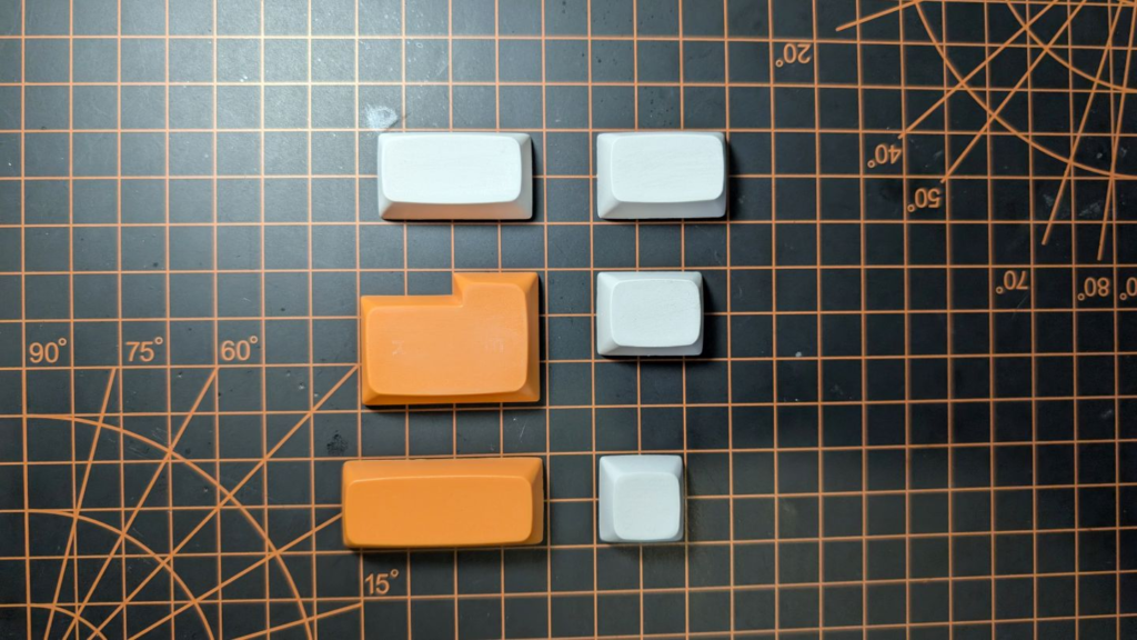 two orange and four white keycaps of different sizes on a cutting pad
