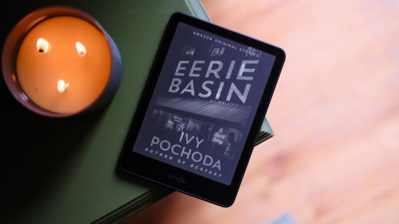 Kindle Paperwhite laying next to lit candle with ebook on screen