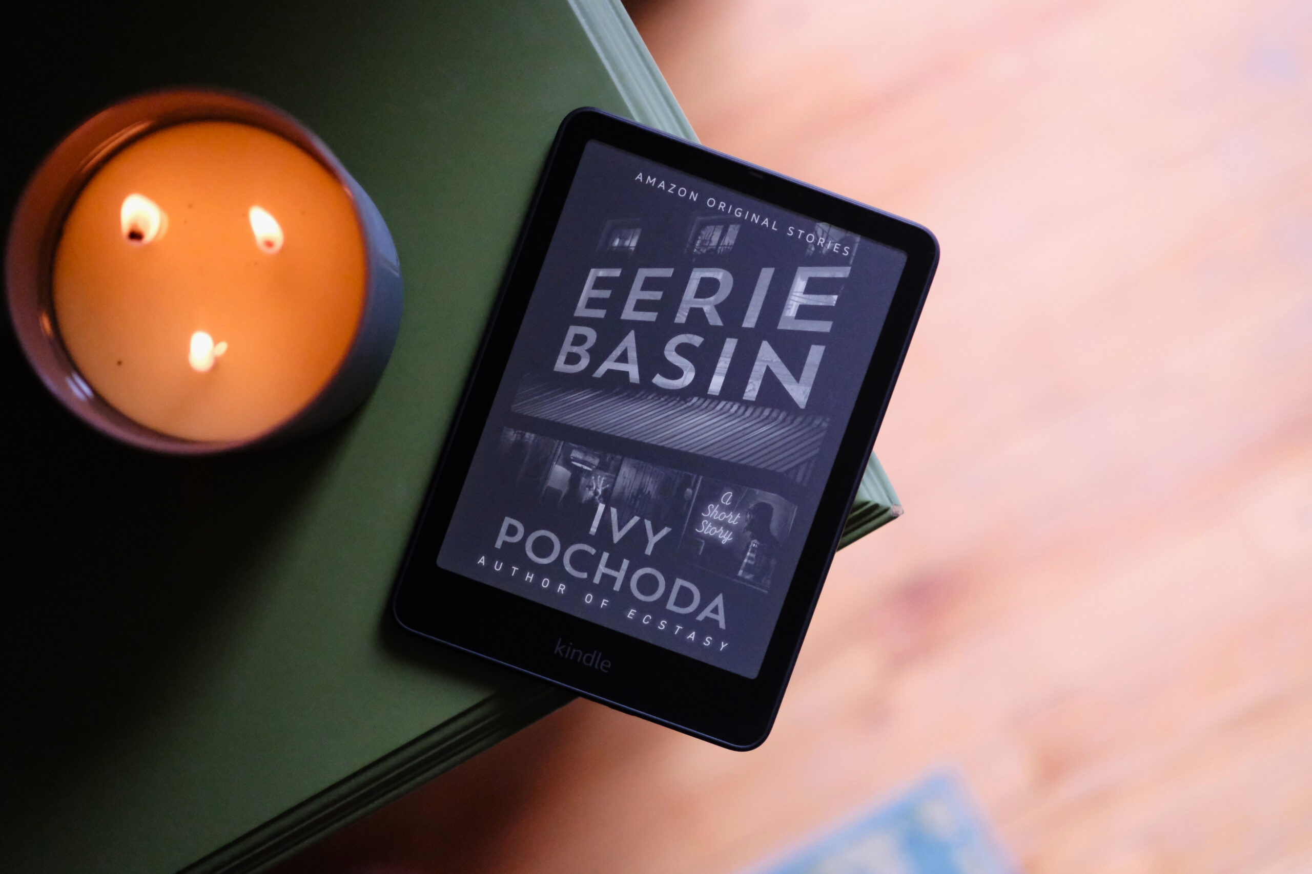 Kindle Paperwhite laying next to lit candle with ebook on screen