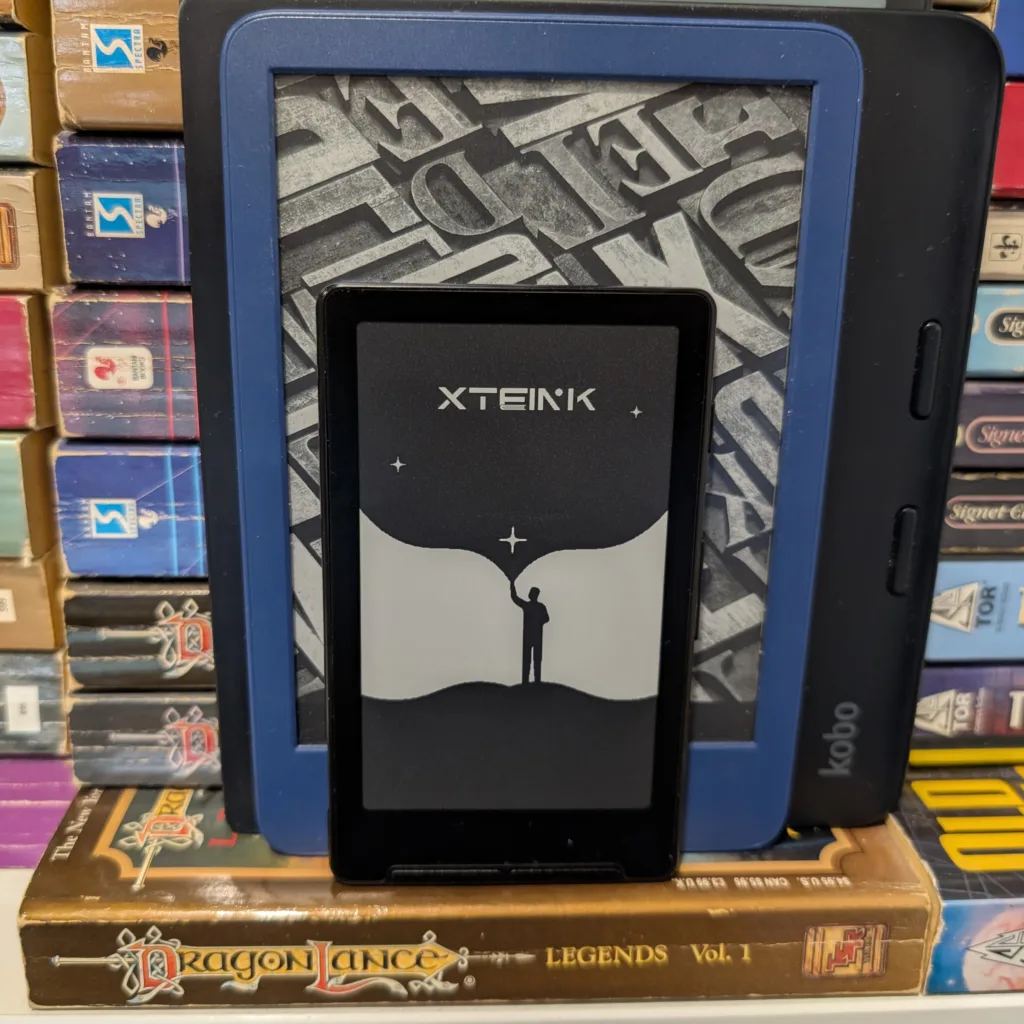 Xteink sitting upright against larger eraders on bookshelf