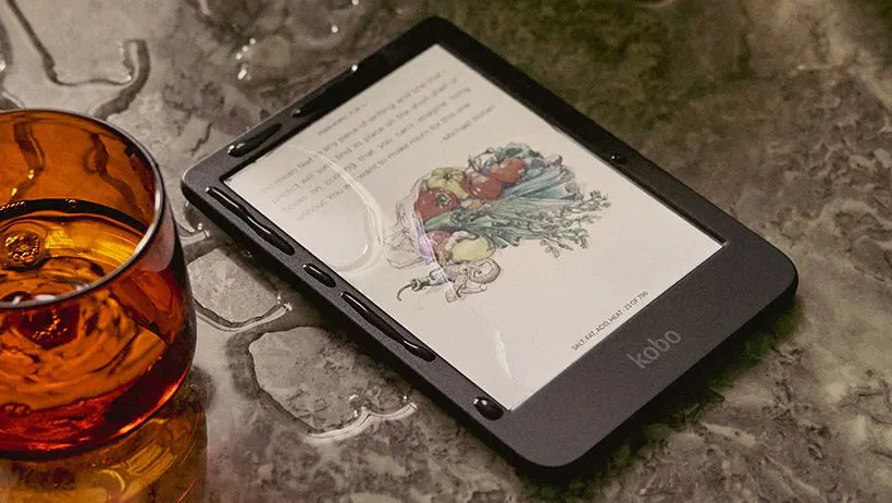Kobo Clara Colour in black on a wet counter top next to a glass tumbler
