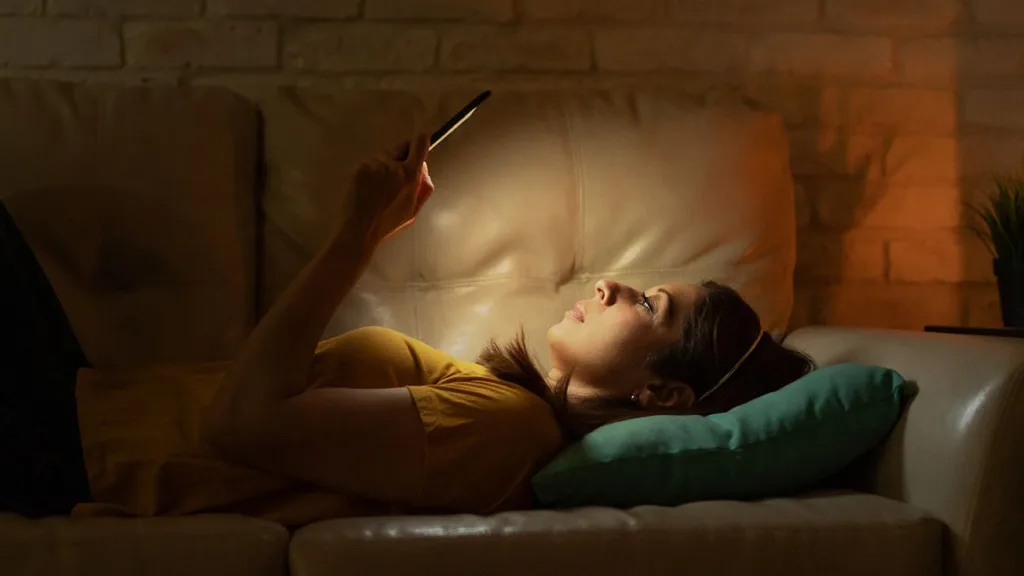 Woman laying on a leather couch reading a black Nook Glowlight 4 in the dark