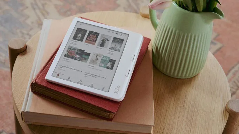 Kobo Libra Colour e-reader on top of books on an end table next to a pitcher with flowers
