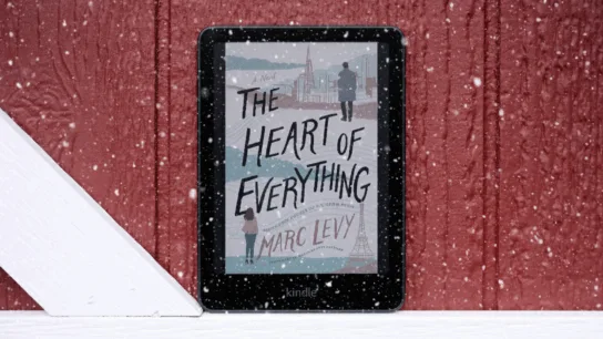 Kindle sitting against red barn door showing book on screen