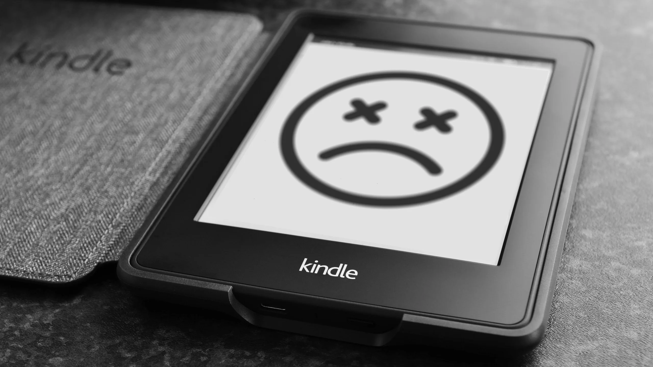Black Kindle e-reader with a sad face emoji with X eyes